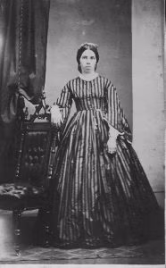 woman standing by post in 1860s clothing